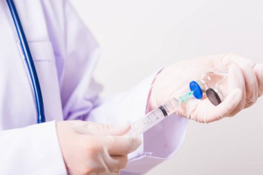 Asyalı kadın doktor ya da hemşire üniformalı ve steteskop takan eldiven takmış. Laboratuvarda elinde şırınga ve ilaç şişesi aşı şişesi, sağlık konsepti olan yüz maskesi takıyor.