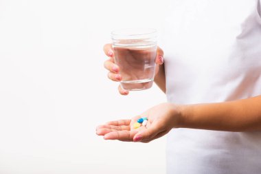 Yakın plan genç Asyalı kadın elinde haplarla hazır bir bardak suyla ilaç alıyor, beyaz arka plan, sağlık ve tıbbi eczane konseptine izole edilmiş stüdyo fotoğrafları çekiyor.