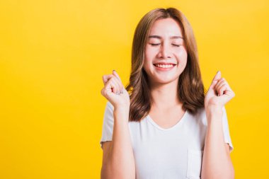 Asya Tayland mutlu portresi ayakta duran güzel hoş genç kadın tişört giyiyor. Yumruklarını kaldırıyor ve galibiyetini kutluyor. Gözlerini kapatıyor.