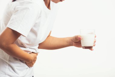 Yakından genç bir kadın hoşgörüsüz, cam sütle el ele tutuşuyor, midesi ağrıyor, laktoza dayanıksızlığı var süt ürünleriyle ilgili sağlıksız bir sorunu var, beyaz arka planda izole edilmiş bir stüdyo çekimi.