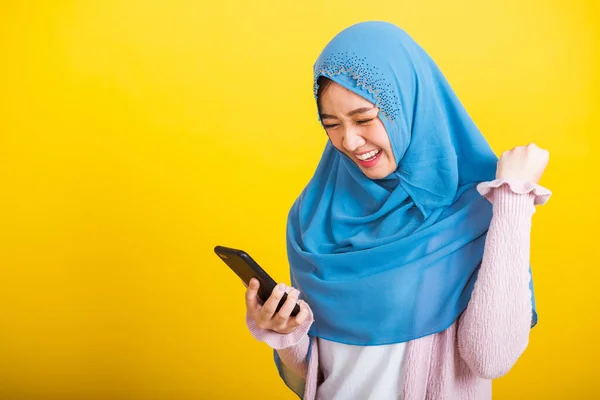 アジア系ムスリムアラブ人 幸せな美しい若い女性の肖像イスラム教の宗教的な摩耗ベールヒジャーブ面白い笑顔彼女は黄色の背景に隔離されたスマート携帯電話で受賞を祝う手を上げる — ストック写真