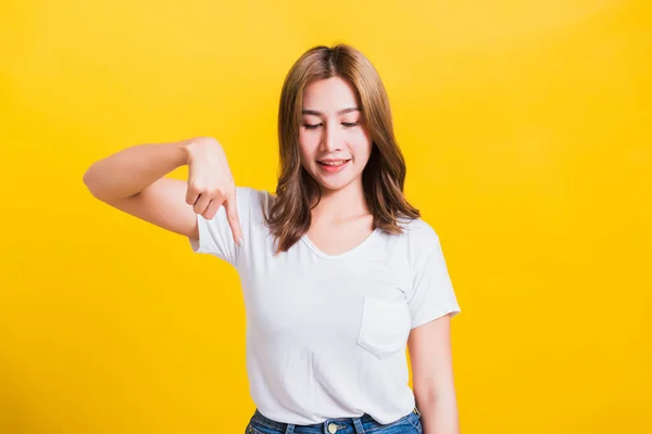 アジアのタイの幸せな肖像画美しいかわいい若い女性立っているTシャツ作るジェスチャー2本の指ポイント下と下を見て スタジオはコピースペースと黄色の背景に隔離されたショット — ストック写真