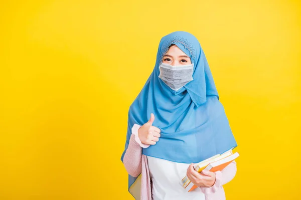 アジア系ムスリムアラブ人 美しい若い女性の肖像宗教的な摩耗ベールヒジャーブと顔のマスク保護コロナウイルスは手に本を保持し 良い兆候のために指親指を表示するには大学に戻る — ストック写真