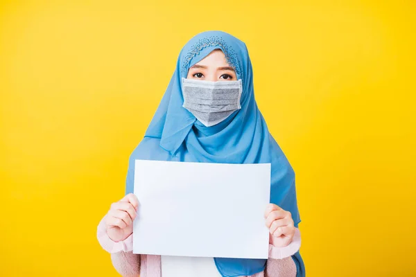 アジアのイスラム教徒のアラブ人 美しい若い女性の肖像宗教的な服のベールヒジャーブと顔のマスク保護コロナウイルスを防ぐために彼女は胸の中に白い紙の空白の板を保持 黄色の背景に隔離 — ストック写真