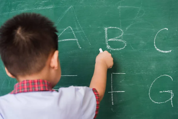 Back to School. Happy Asian funny back of cute little child boy kindergarten preschool in student uniform writing ABC with white chalk on green school blackboard, First time to school education