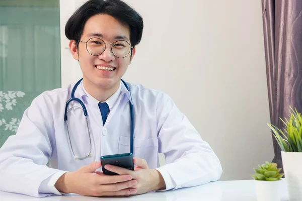 アジアの医師の若いハンサムな男は 病院のデスクオフィスでデジタルスマートフォンでの作業や保持を使用して笑顔 技術医療の概念 — ストック写真