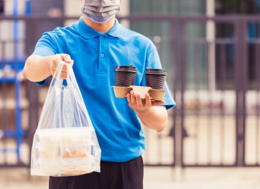 Mavi üniformalı Asyalı genç teslimatçı market servisi yapıyor. Salgın koronavirüs altında evdeki pirinç kutularına plastik torbalar ve kahve veriyor. Yeni normal konsepte geri dönüyoruz.