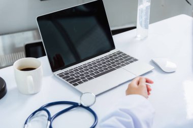 Tıp doktoru masabaşında çalışıyor. Stetoskop 'a yakın çekim. Asyalı kadın hekimin eli hastalara hastane ofisindeki dizüstü bilgisayarın önünde sağlık sigortası konseptini açıklıyor.