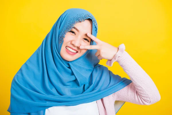アジア系ムスリムアラブ人 幸せな美しい若い女性の肖像イスラム教の宗教的な摩耗ベールヒジャーブの笑顔彼女はジェスチャーを示す手2本の指Vサインシンボル目の近くに隔離された黄色の背景 — ストック写真