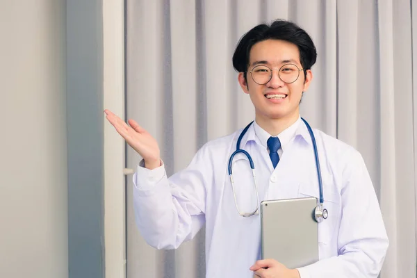 幸せなアジアの若い医師の肖像画の閉鎖ハンサムな男笑顔で制服と聴診器首ストラップ手にスマートデジタルタブレットを保持し 離れて手を示す 医療医学の概念 — ストック写真