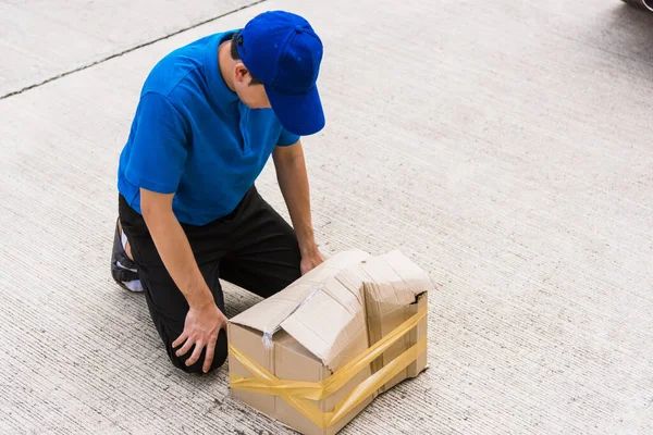 身穿蓝色制服的亚洲年轻人送货员情绪低落的送货员持着破损的纸板箱在家门口被砸坏了 意外导致运输不良或送货上门服务质量差 — 图库照片