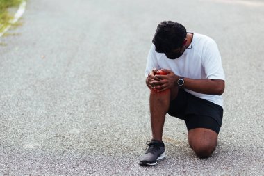 Kapatın Asyalı genç spor koşucusu. Siyah adam, el ele oturuyor. Açık hava sokak sağlık parkında koşarken diz ağrısı çekiyor.