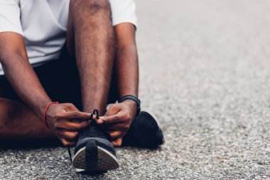 Asyalı spor koşucusu, ayakkabı bağcığında oturan, koşuya hazırlanan ve dışarıda koşan siyah adam, sağlık egzersizi konsepti.