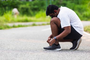 Kapatın Asyalı spor koşucusu siyah adam kol saati takıyor ayakkabı bağcığı deniyor koşuya hazırlanıyor ve sağlık parkında koşuyor, sağlıklı egzersiz konsepti.