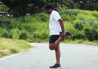 Kapatın Asyalı genç atlet spor koşucusu siyah adam kol saati takın bacaklarınızı ve dizlerinizi esnetin açık hava sokak sağlık parkında koşmadan önce spor konseptinden önce sağlıklı egzersiz