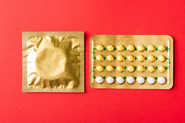 World sexual health or Aids day, condom on wrapper pack and contraceptive pills blister hormonal birth control pills, studio shot isolated on a red background, Safe sex and reproductive health concept