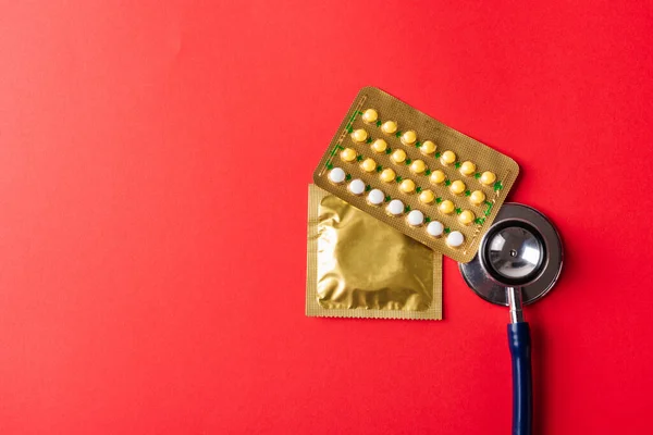 World sexual health or Aids day, Top view flat lay condom in wrapper pack, birth control pill and doctor stethoscope, studio shot isolated on a pink background, Safe sex and reproductive health concept