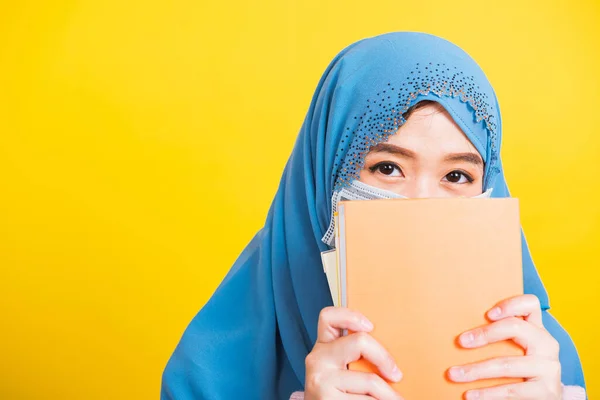 Asian Muslim Arab, Happy beautiful young woman religious wear veil hijab and face mask to prevent coronavirus she student hold books close face, isolated on yellow background, Back to college