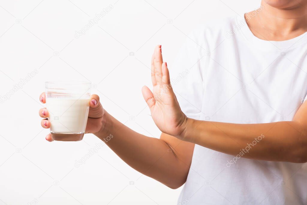 Closeup woman raises a hand to stop sign use hand holding glass milk she is bad stomach ache has bad lactose intolerance unhealthy problem with dairy food, studio shot isolated on white background