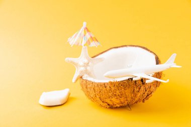 Mutlu hindistan cevizi günü konsepti, taze hindistan cevizi, deniz yıldızı, uçak, güneş şemsiyesi, sarı arka planda izole edilmiş stüdyo çekimi, plaj tropikal meyve yolculuğu ve bahar tatili