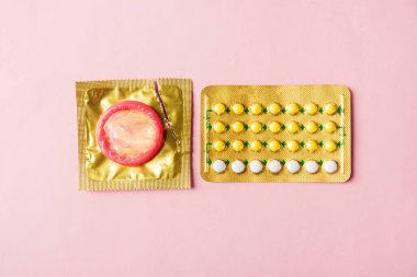 Dünya seks sağlığı ya da AIDS günü, prezervatif paketi ve doğum kontrol hapları hormonal doğum kontrol hapları, pembe arka planda izole edilmiş stüdyo çekimi, güvenli seks ve üreme sağlığı konsepti.