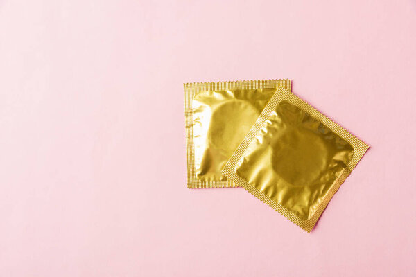 World sexual health or Aids day, Top view flat lay condom in wrapper pack, studio shot isolated on a pink background, Safe sex and reproductive health concept