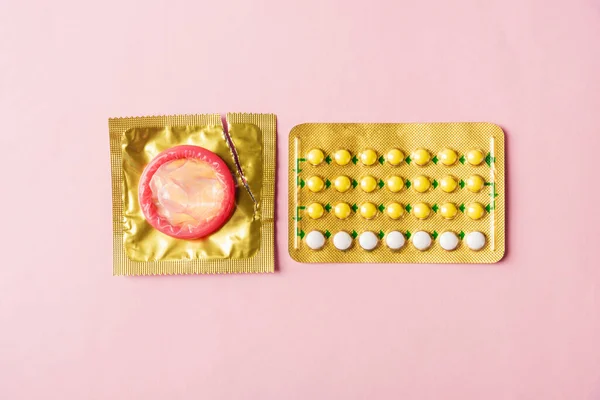 World sexual health or Aids day, condom on wrapper pack and contraceptive pills blister hormonal birth control pills, studio shot isolated on a pink background, Safe sex and reproductive health concept