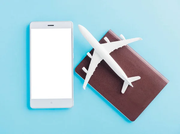 World Tourism Day, Top view flat lay of minimal toy model plane, airplane on passport and mobile smartphone blank screen, studio shot isolated on a blue background, accessory flight holiday concept