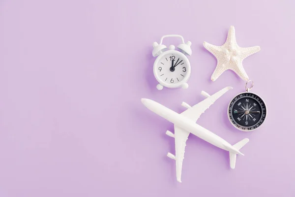 世界観光デー 最小限のおもちゃモデル飛行機 飛行機 ヒトデ 目覚まし時計とコンパスのトップビューの平らなレイアウト 紫色の背景に隔離されたスタジオショット アクセサリーフライト休日のコンセプト — ストック写真