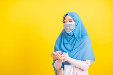 Asyalı Müslüman Arap, portre güzel genç kadın başörtüsü takıyor ve yüz maskesi takıyor. Koronavirüsü önlemek için kına ile süslenmiş, Allah 'a dua ediyor, sarı arka planda izole edilmiş.