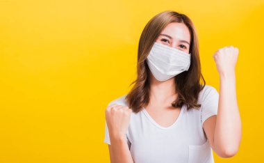 Yüz maskesi takan Asyalı güzel genç kadın toz filtresi pm2.5, COVID virüsü ve hava kirliliği sarı arka planda hastalıktan kurtulduktan sonra sevinçten havalara uçtu.