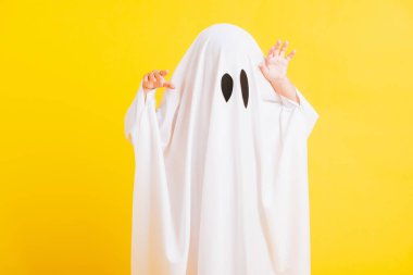 Komik cadılar bayramı çocuğu kavramı, yakın plan beyaz kostümlü küçük şirin çocuk cadılar bayramı hayaleti korkunç, sarı arka planda izole edilmiş stüdyo resmi.