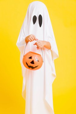 Komik cadılar bayramı çocuğu kavramı, beyaz kostümlü şirin çocuk Cadılar Bayramı hayaleti korkunç elinde turuncu kabak hayaleti, beyaz arka planda sarı bir stüdyo.