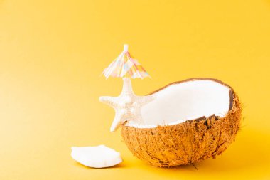 Mutlu hindistan cevizi günü konsepti, taze hindistan cevizi, deniz yıldızı ve güneş şemsiyesi, sarı arka planda izole edilmiş stüdyo çekimi, plaj tropikal meyve bahar tatili