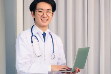 Doktor elbisesi giyen ve steteskop gülümseyen Asyalı genç doktor portresi, sağlık hizmetleri konsepti.
