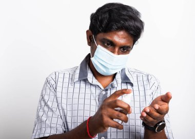 Gözlerinde koruyucu yüz maskesi olan Asyalı siyah adam, beyaz arka planda izole edilmiş dezenfektan spreyi, hijyen önleme COVID-19 virüsü veya koronavirüs koruma kavramı gösteriyor.