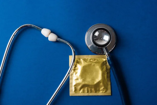 World sexual health or Aids day, Top view flat lay medical equipment, condom in pack and stethoscope, studio shot isolated on dark blue background, Safe sex and reproductive health concept