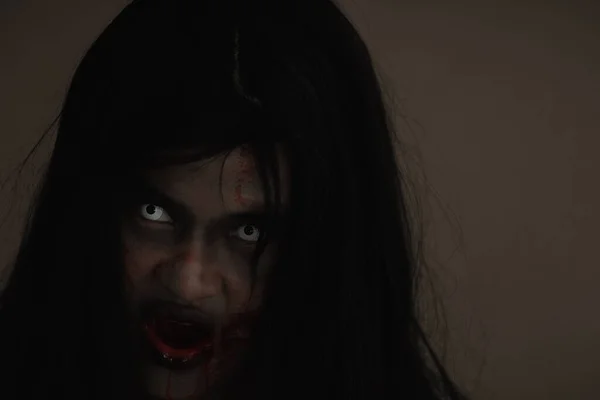 Girl zombie in blood. Closeup face and eyes of Asian Woman ghost with blood. Horror creepy scary fear in a dark house. Hair covering the face, Halloween festival concept