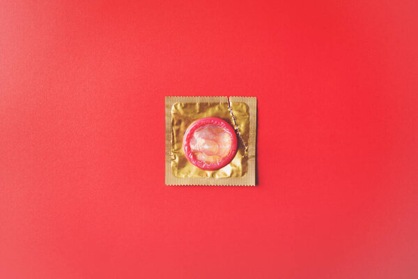 World sexual health or Aids day, Top view flat lay condom in wrapper pack is tear open, studio shot isolated on a red background, Safe sex and reproductive health concept