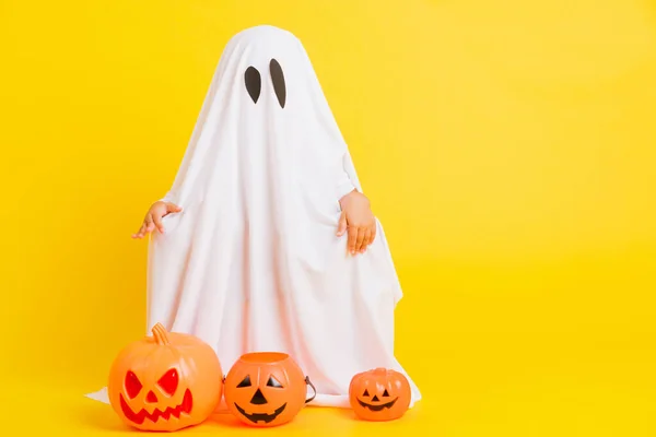 Funny Halloween Kid Concept, full body of a little cute child with white dressed costume halloween ghost scary he holding orange pumpkin ghost, studio shot yellow on white background