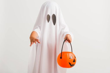 Komik Cadılar Bayramı Çocuğu kavramı, beyaz kostümlü küçük şirin çocuk Cadılar Bayramı hayaleti korkunç elinde turuncu kabak hayaleti, beyaz arka planda tek başına çekilmiş bir stüdyo resmi.