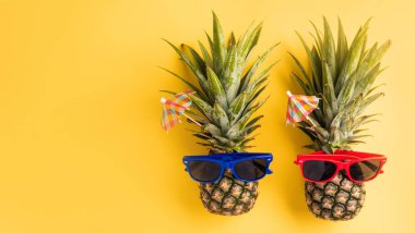 Yaz Ananas Günü Konsepti, Güneş gözlüklü iki ananas yatağı, sarı arka planda izole edilmiş stüdyo çekimi, tropikal yaz tatili