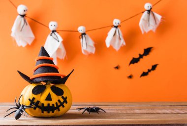 Komik Cadılar Bayramı dekorasyon partisi, şirin balkabağı hayaleti hayalet kabak fener maskesi şapka, siyah örümcek ve yarasalar ahşap masada, stüdyo çekimi turuncu arka planda, mutlu bayramlar konsepti