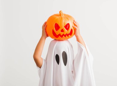 Komik Cadılar Bayramı Çocuğu kavramı, beyaz kostümlü küçük şirin çocuk Cadılar Bayramı hayaleti korkunç elinde turuncu kabak hayaleti, beyaz arka planda tek başına çekilmiş bir stüdyo resmi.