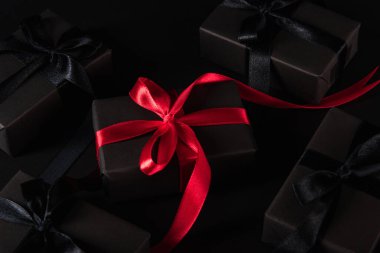 Kara Cuma alışverişi konsepti, hediye kutusunun üst görüntüsü siyah kağıt ve siyah kurdeleyle kaplanmış kutunun etrafında kırmızı kurdele, arka planda stüdyo çekimi.