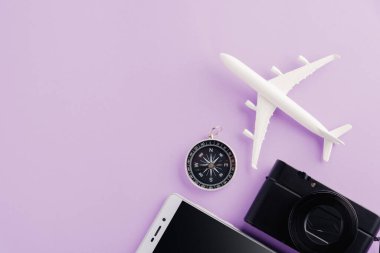 Dünya Turizm Günü, minimum model uçak, uçak, denizyıldızı, alarm saati, pusula, kamera ve akıllı telefon görüntüsü, mor arka planda izole edilmiş stüdyo görüntüsü, aksesuar uçuş tatil konsepti
