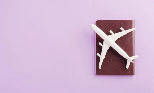 World Tourism Day, Top view flat lay of minimal toy model plane, airplane on passport, studio shot isolated on a purple background, accessory flight holiday concept