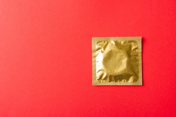 World sexual health or Aids day, Top view flat lay condom in wrapper pack, studio shot isolated on a red background, Safe sex and reproductive health concept