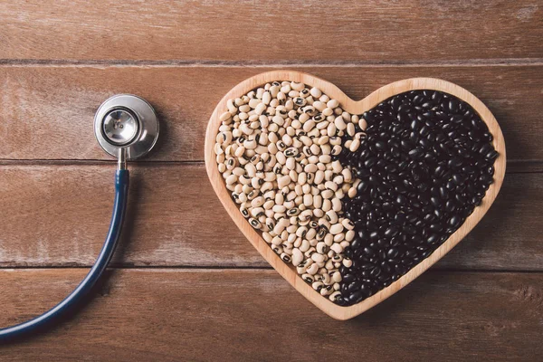 World food day, black bean and soybean seeds or white cowpea beans on a heart plate and doctor stethoscope on wooden background, studio shot