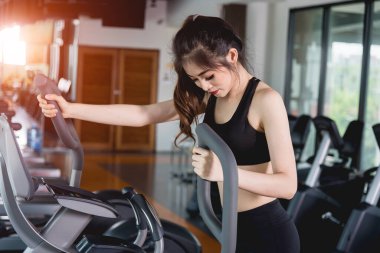 Genç kadın yaşam tarzı spor salonunda kardiyo çalışması için makine eliptik kullanıyor.